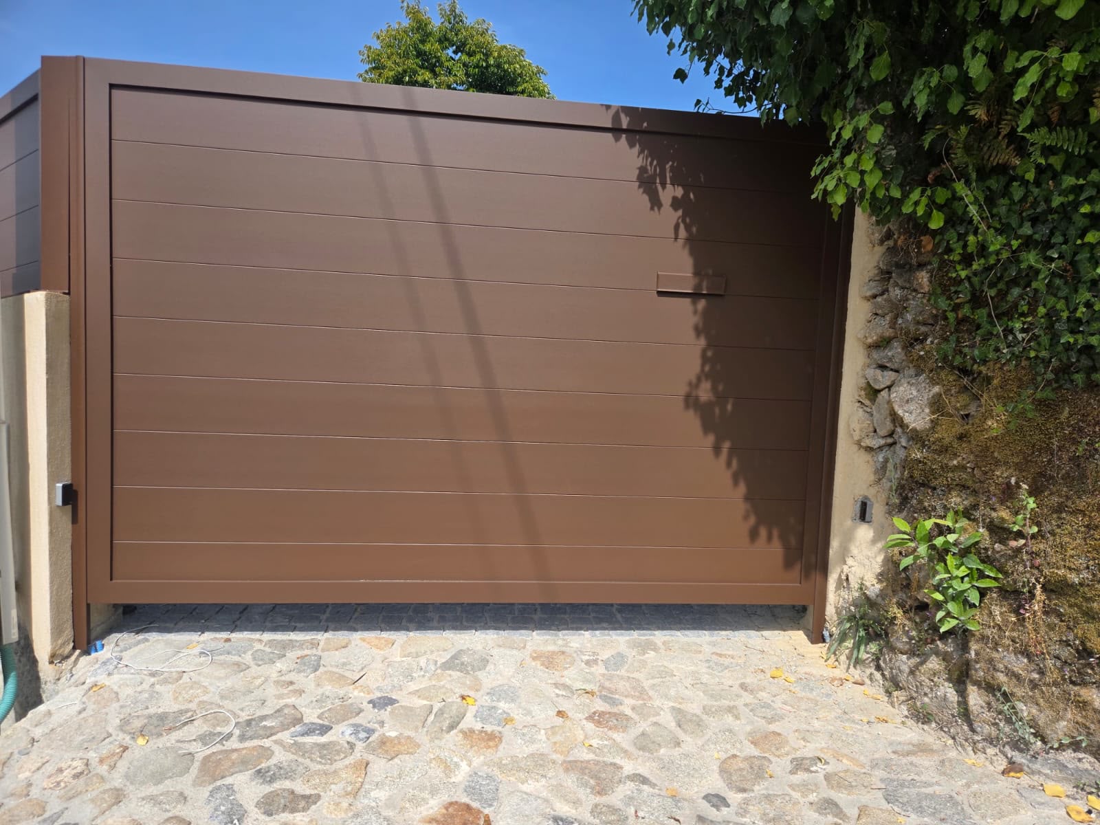 Portão castanho à medida instalado numa entrada em pedra